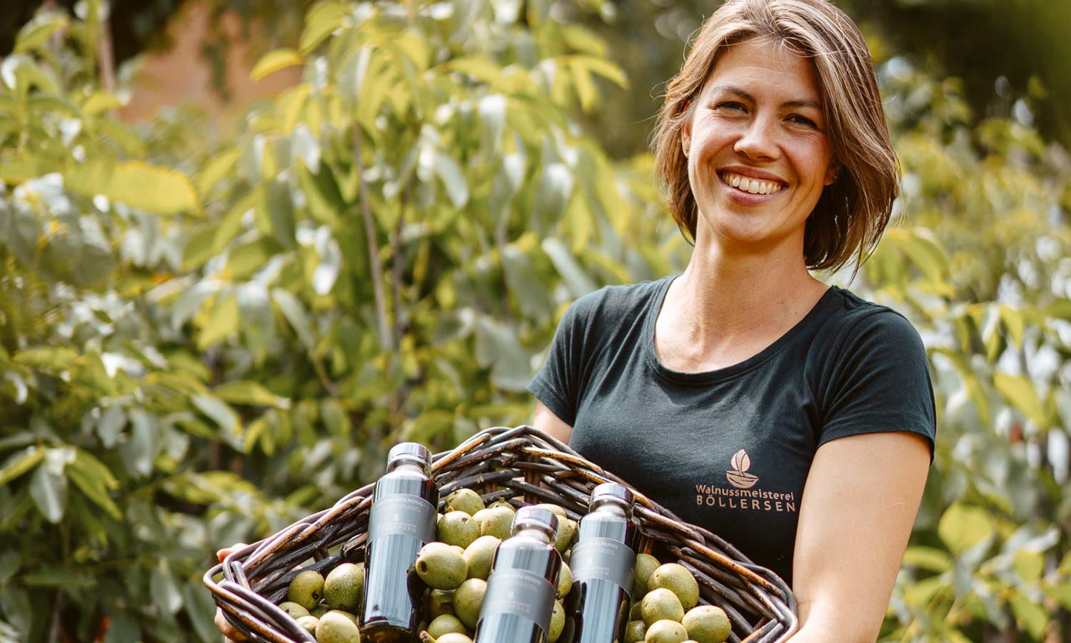 Vivian Böllersen, Inhaberin der Walnussmeisterei, trägt lächelnd einen Korb mit grünen Walnüssen und Walnussöl und blickt direkt in die Kamera.