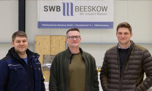 Dieses Foto zeigt die drei Geschäftsführer der Firma Stahlwasserbau-Beeskow gemeinsam vor ihrem Firmenschild mit dem Firmenlogo darauf und dient als Titelbild für den Beitrag 'Erfolgsgeschichte' der Bürgschaftsbank Brandenburg "Gelungene Generationenübergabe mit Unterstützung der Bürgschaftsbank in Beeskow"