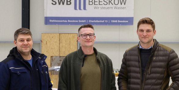 Dieses Foto zeigt die drei Geschäftsführer der Firma Stahlwasserbau-Beeskow gemeinsam vor ihrem Firmenschild mit dem Firmenlogo darauf und dient als Titelbild für den Beitrag 'Erfolgsgeschichte' der Bürgschaftsbank Brandenburg "Gelungene Generationenübergabe mit Unterstützung der Bürgschaftsbank in Beeskow"