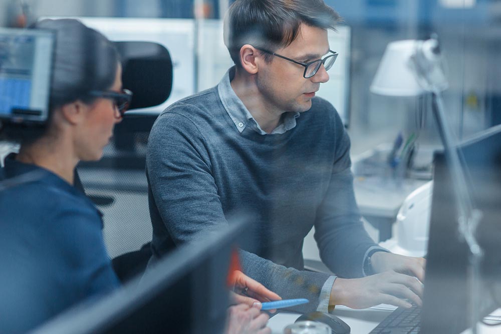 Das Bild zeigt einen Mann und eine Frau die in sehr technischer Umgebung auf einen Monitor schauen und sich konzentriert unterhalten und dient als Beitragsbild für den Beitrag Rückblick und Ausblick der Wirtschaft in Brandenburg von der Bürgschaftsbank Brandenburg.